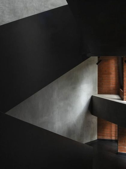 An intimate view of the Brick House staircase, where the dark, angular forms are juxtaposed against the warm texture of the brick wall.