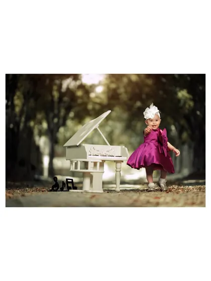 A dramatic and beautiful portrait of a little girl in a vibrant magenta dress, pointing excitedly from her miniature piano in a tree-lined lane.