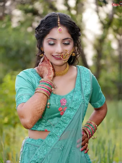 A beautiful portrait taken in a natural, green setting. The model's teal lehenga and traditional jewelry stand out, while her gentle pose conveys a sense of peace and elegance.