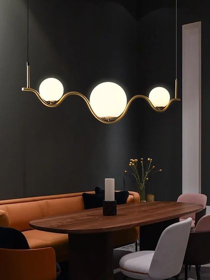 The wavy globe pendant light looks fantastic over a long dining table in a room with dark, moody walls. The warm light from the globes creates an intimate and inviting atmosphere.
