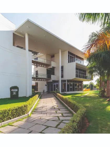 The entrance to the office building is marked by a large, double-height volume supported by slender columns. This creates a welcoming, shaded transition space, with a stone pathway leading through landscaped gardens.