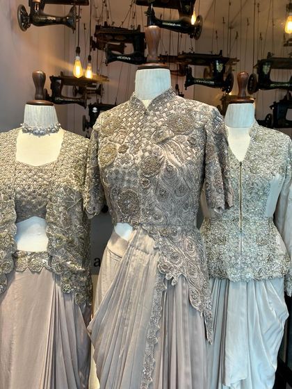 A trio of couture outfits in a sophisticated grey palette, showcasing a pre-draped saree, a jacket set, and a crop top with a skirt, all heavily embroidered.