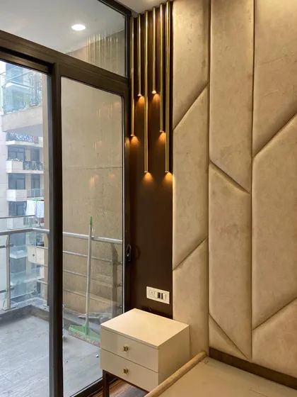 Another view of the custom headboard design, showing its relationship to the room's architecture. The large glass door to the balcony allows natural light to flood the space, highlighting the textures of the upholstered wall panels.