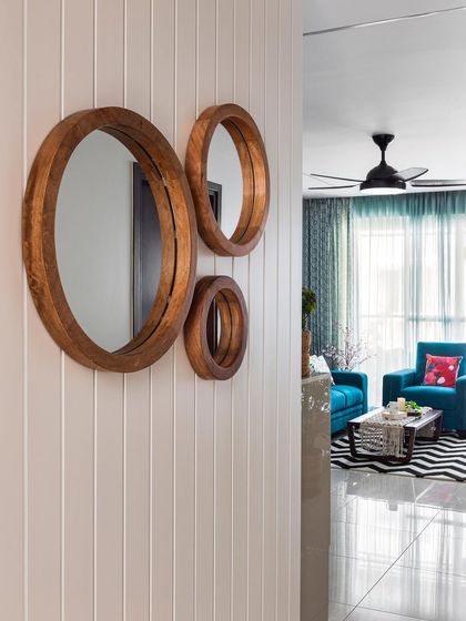 A simple and elegant entryway featuring a trio of round wooden mirrors on a white vertically paneled wall. This design creates a warm and welcoming first impression while adding texture and interest to the foyer.
