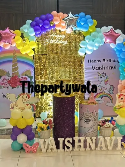A grand unicorn party with a rainbow balloon arch and a gold shimmer wall. The setup includes multiple themed pedestals and large unicorn balloon sculptures.