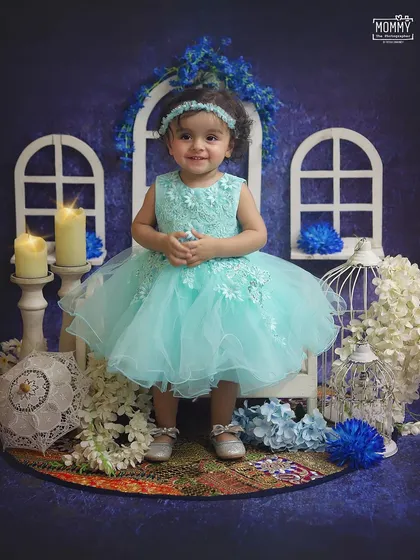 A vision in blue! This sweet little girl is all smiles in our dreamy blue-themed studio setup, complete with white window props, candles, and flowers.