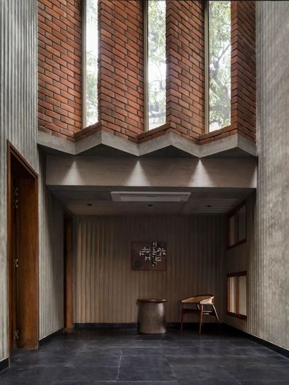 The entrance foyer of the Brick House sets a contemplative tone. Fluted concrete walls, black stone flooring, and strategically placed brickwork create a rich textural experience, animated by light from the staggered windows above.