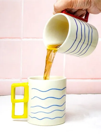 An action shot of tea being poured between two artistic, modern mugs, highlighting their unique design.