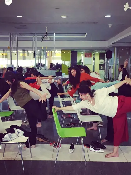 Using chairs for support in a balancing pose. This makes yoga accessible to everyone in the office, regardless of their flexibility or experience level.