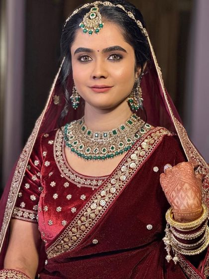 A close-up portrait of the bride. Her eyes are defined with a soft smoke, and the skin is kept luminous to balance the heavy emerald jewelry.