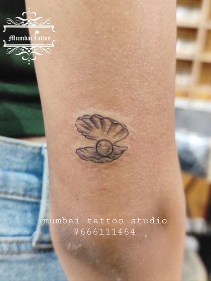 A small, detailed tattoo of a pearl in an oyster shell. This design symbolizes hidden beauty and wisdom, crafted with fine lines to capture its delicate nature.