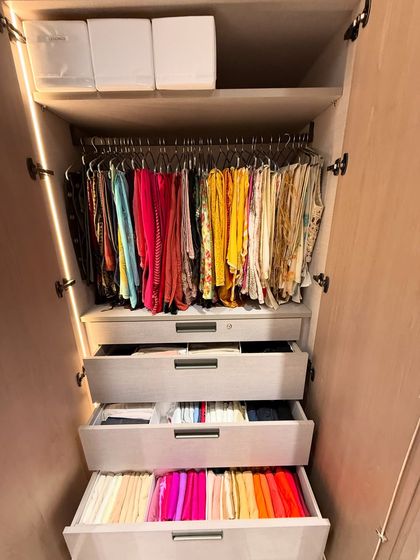 A vibrant collection of dupattas and scarves hanging above drawers filled with color-coded, vertically folded items.