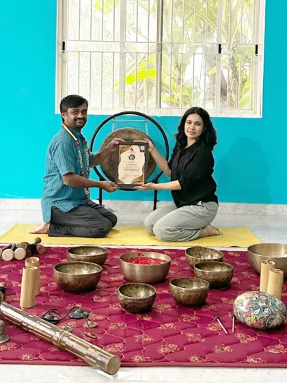 A student receives his certificate in front of a large gong, another powerful instrument we explore in our sound healing workshops.