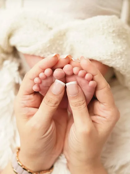 A mother's hands with a perfect manicure gently hold her baby's tiny feet. This is a beautiful way to include a touch of mom's personality in the detail shots.