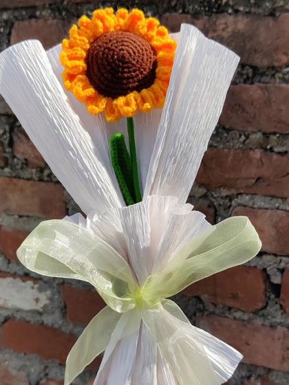 The single sunflower bouquet held against a brick wall background.