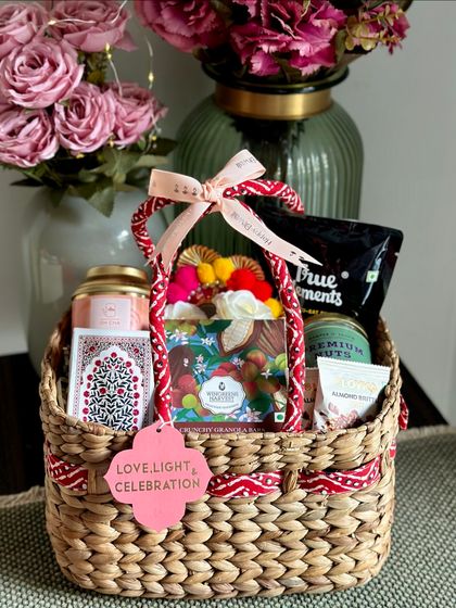 Love, Light, and Celebration. This festive basket is curated with a deck of playing cards, Oh Cha tea, a seed mix, granola bars, and premium nuts, making it a wonderful gift for enjoying festive evenings with family.