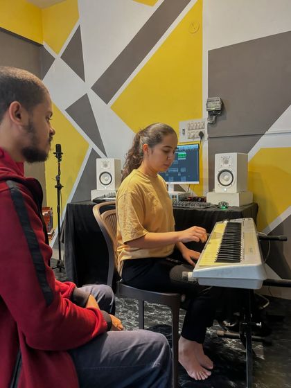 Our instructor observes as a student practices on the keyboard, with professional studio monitors and equipment in the background.