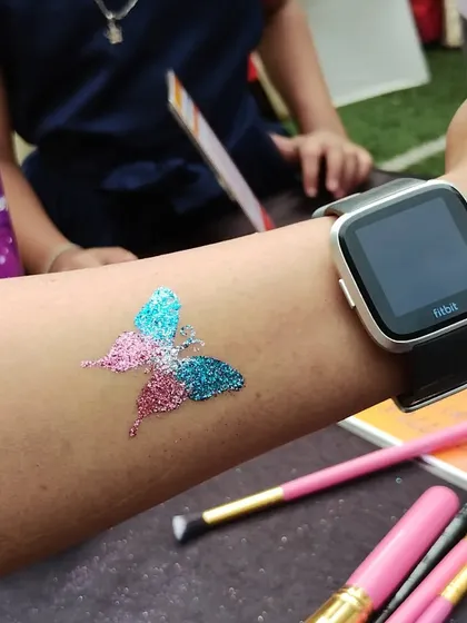 Here is a behind-the-scenes look at my setup. This multi-colored butterfly glitter tattoo is freshly applied, with my professional brushes and skin-safe glitter pots ready for the next happy customer.