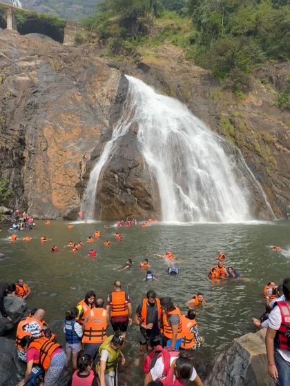 A wide shot showing many people enjoying the large natural pool at the bottom of Dudhsagar falls.