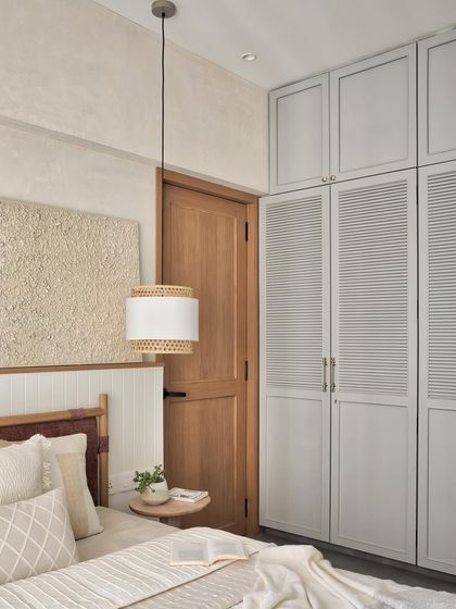 Pendant lamps crafted from cane and fabric illuminate the space, while custom wardrobes with louvered and matte grey finishes provide ample storage. The design is both beautiful and practical.