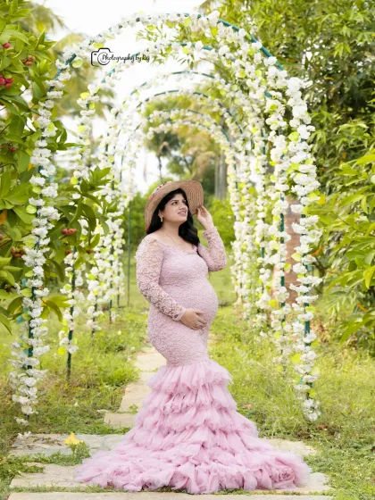 A beautiful solo portrait under a floral archway. The mother-to-be is wearing a pink lace gown and a hat.