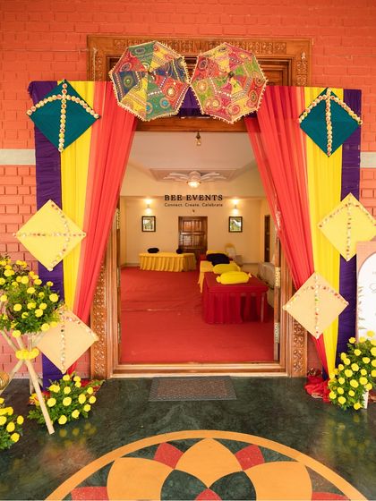 A vibrant entrance decor for a Mehendi ceremony. The colorful drapes, kite decorations, and marigold flower arrangements create a festive and welcoming pathway for guests.