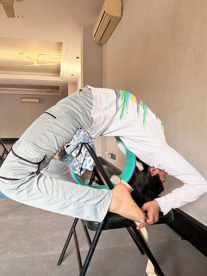 We use props to help students achieve their flexibility goals. This student is using a chair to support their body in a deep backbend and split variation, allowing them to hold the stretch and open the hips and spine.