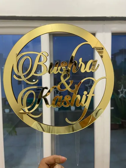 A circular topper featuring the names "Bushra & Kashif" in an elegant, overlapping script.
