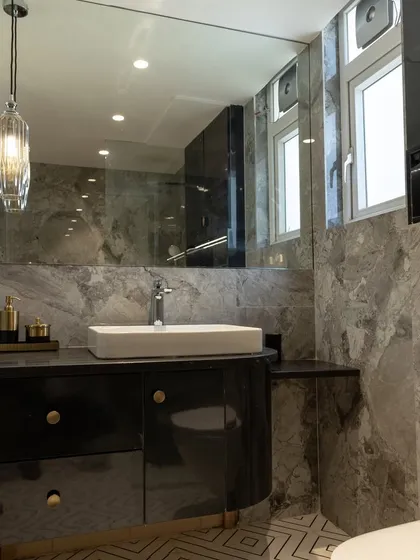 The vanity area of this modern bathroom combines a glossy black cabinet with a white vessel sink and elegant pendant lighting. A large, frameless mirror enhances the sense of space and light.