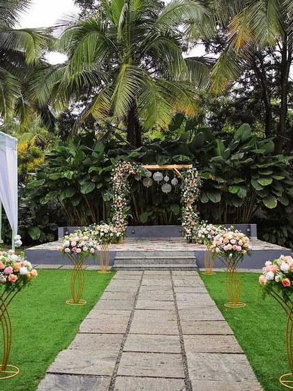 A simple and elegant ceremony setup. The floral arch with hanging lanterns is placed on the stage, with the lush lawn and trees providing a beautiful natural setting.