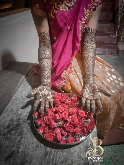 A beautiful shot of a bride's hands, adorned with custom portrait henna, held over a plate of fresh roses. This image captures the romance and tradition of bridal mehndi.