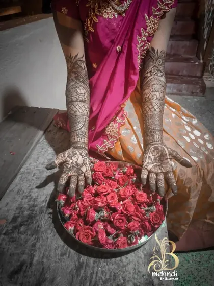 A beautiful shot of a client's hands, adorned with intricate mehndi, held over a plate of roses.