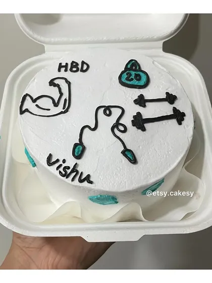 A fitness-themed birthday bento cake for 'Vishu', decorated with drawings of a bicep, kettlebell, dumbbells, and a skipping rope.