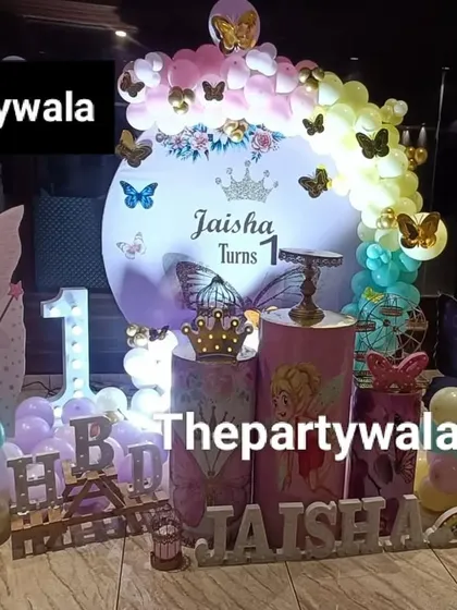 A whimsical fairy tale theme with a custom photo board. The pastel rainbow balloon arch and fairy cutouts create a magical atmosphere for a first birthday.