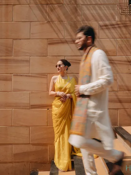 A dynamic and editorial-style shot from a Haldi ceremony. The motion blur of the groom walking past the poised bride creates a sense of story and movement, capturing the vibrant energy of the day.