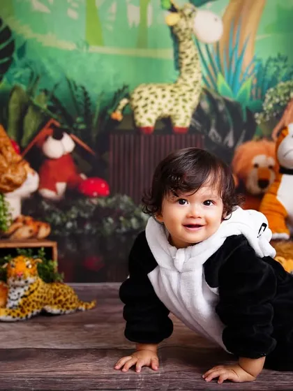 A happy baby in a panda costume crawling through a jungle-themed setup filled with his favorite stuffed animals.