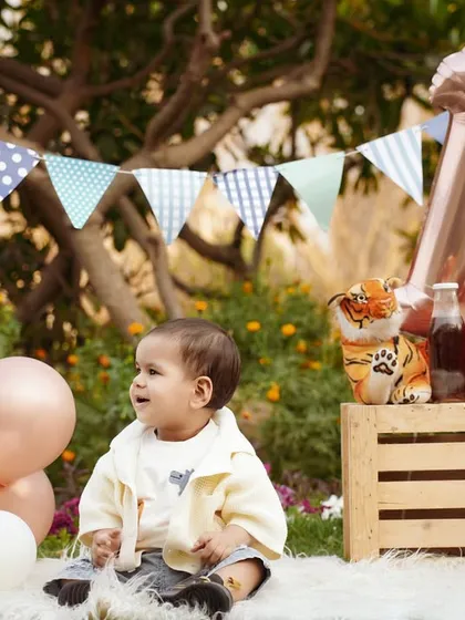 A charming outdoor first birthday picnic. The setup with bunting, balloons, and a crate of juice bottles creates a relaxed and festive vibe.
