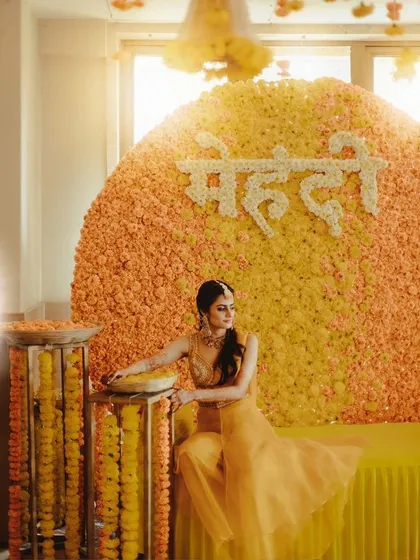 A truly enchanting mehendi moment. The bride poses against a massive circular backdrop made entirely of yellow and orange marigolds.
