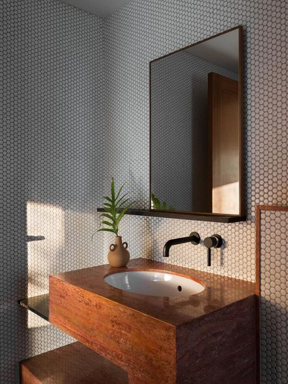 This guest bathroom features a custom vanity made from red travertine. The warm, earthy tones of the stone are paired with minimalist black fixtures, creating a space that is both rustic and modern.