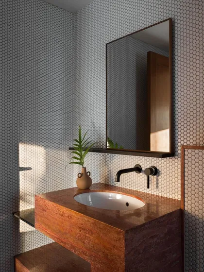 This guest bathroom features a custom vanity made from red travertine. The warm, earthy tones of the stone are paired with minimalist black fixtures, creating a space that is both rustic and modern.