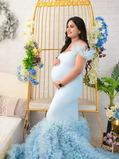 A portrait of a queen on her throne. Seated in our popular golden birdcage chair, this mother-to-be looks radiant in a light blue ruffled gown, surrounded by delicate floral arrangements.