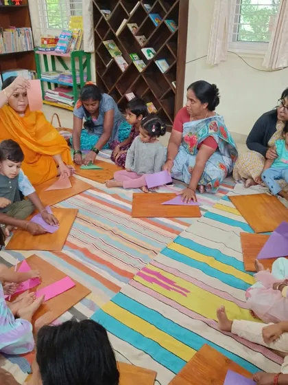 The storyteller helps the children with their paper crafts, ensuring everyone can participate and succeed.
