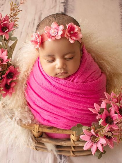 A newborn "rose" sleeping in a basket. This setup uses a pink wrap and floral props to create a beautiful garden theme.