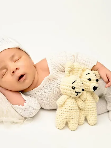 A vision in white. This newborn sleeps peacefully on a simple white background, holding two tiny teddy bears, creating a pure and timeless image.