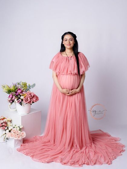 A classic full-length solo portrait. The mom-to-be is glowing in a beautiful pink tulle gown, surrounded by soft floral arrangements in the studio.