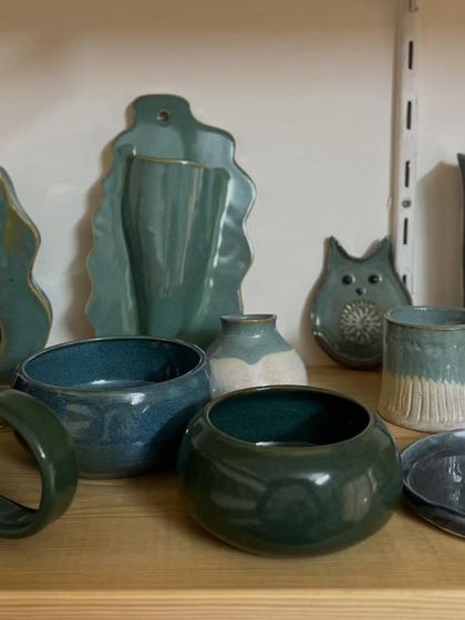 A beautiful collection of student pieces in shades of green and blue, fresh out of the kiln. The glaze transforms them from plain clay into functional art.
