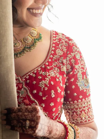 A close-up of our bride's stunning necklace, peeking out to complement her intricately embroidered red lehenga. It's all in the details.