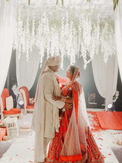 The color version of the same portrait, showing the contrast between the bride's red lehenga and the white decor. It's a beautiful, romantic wedding shot.