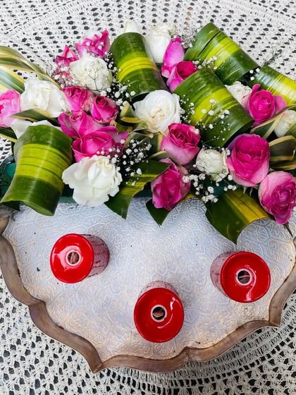 This floral urli bowl showcases a creative arrangement of pink and white roses with folded leaves. The addition of the three small red candle holders adds a pop of contrasting color and a place for gentle light.