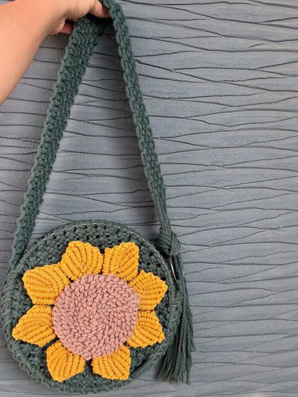 Holding up our handmade sunflower sling bag. It's a round, spacious design with a comfortable strap and a tassel detail, combining boho style with practical use.
